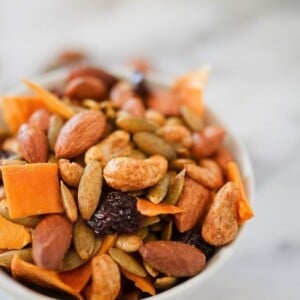 A white bowl filled with dried mango, nuts, seeds, and raisins, covered in curry spices.