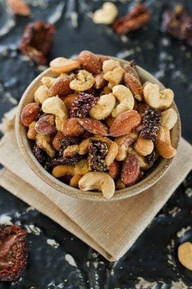 Pizza Trail Mix in a bowl, on top of a folded cloth napkin. Trail mix make from mixed nuts and dried tomatoes with seasoning.