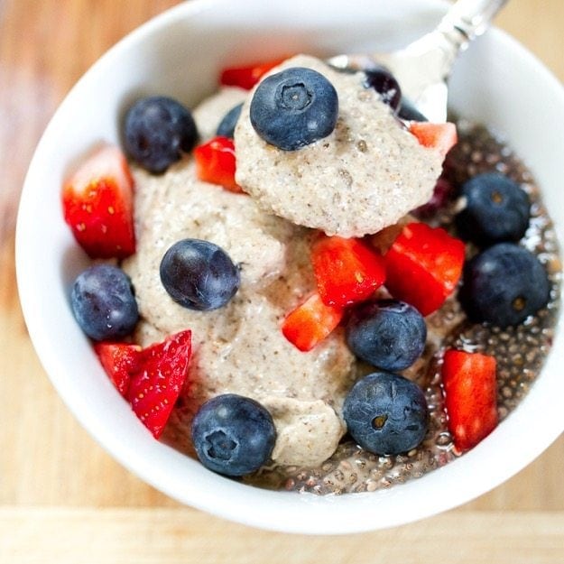 A spoonful of chia pudding above a bowl, topped with blueberry and strawberry.