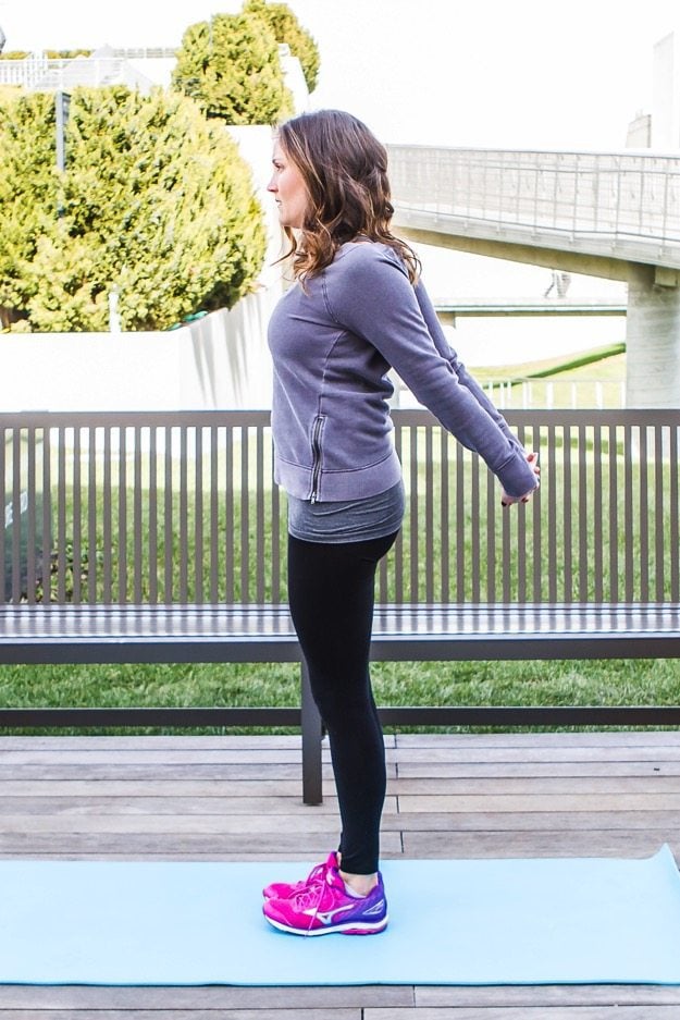 Girl standing on yoga mat doing chest opener stretch. 