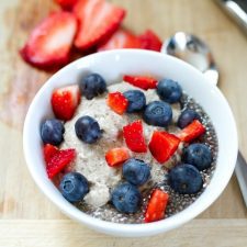 A bowl of creamy cashew chia pudding topped with blueberries and chunks of strawberry.
