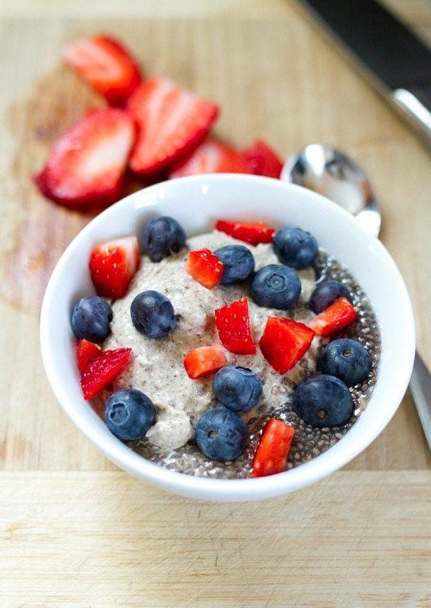 A bowl of creamy cashew chia pudding topped with blueberries and chunks of strawberry.