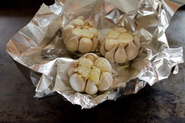 Three heads of garlic sitting on aluminum foil. 