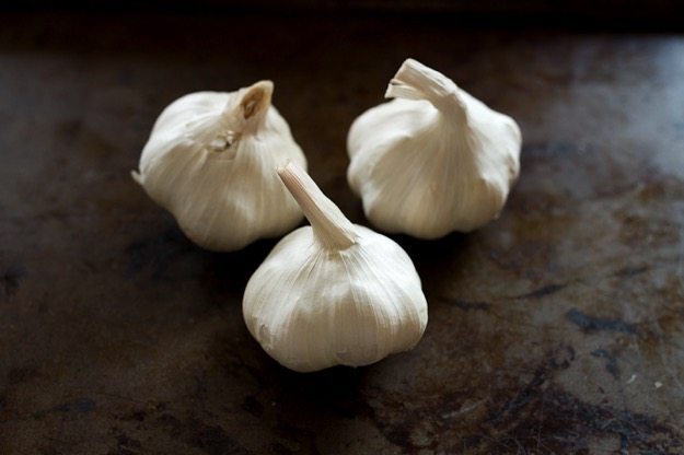Three heads of garlic sitting on a baking sheet. 