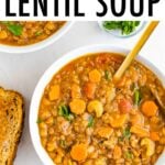 Bowl of lentil soup with celery and carrots. Beside the bowl is a slice of bread and parsley.