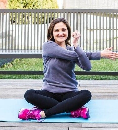 Girl sitting on yoga mat doing a shoulder stretch.