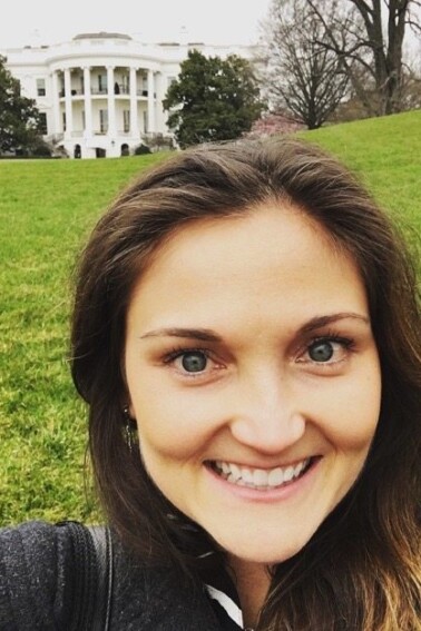 A woman with dark hair smiling in front of the whitehouse.