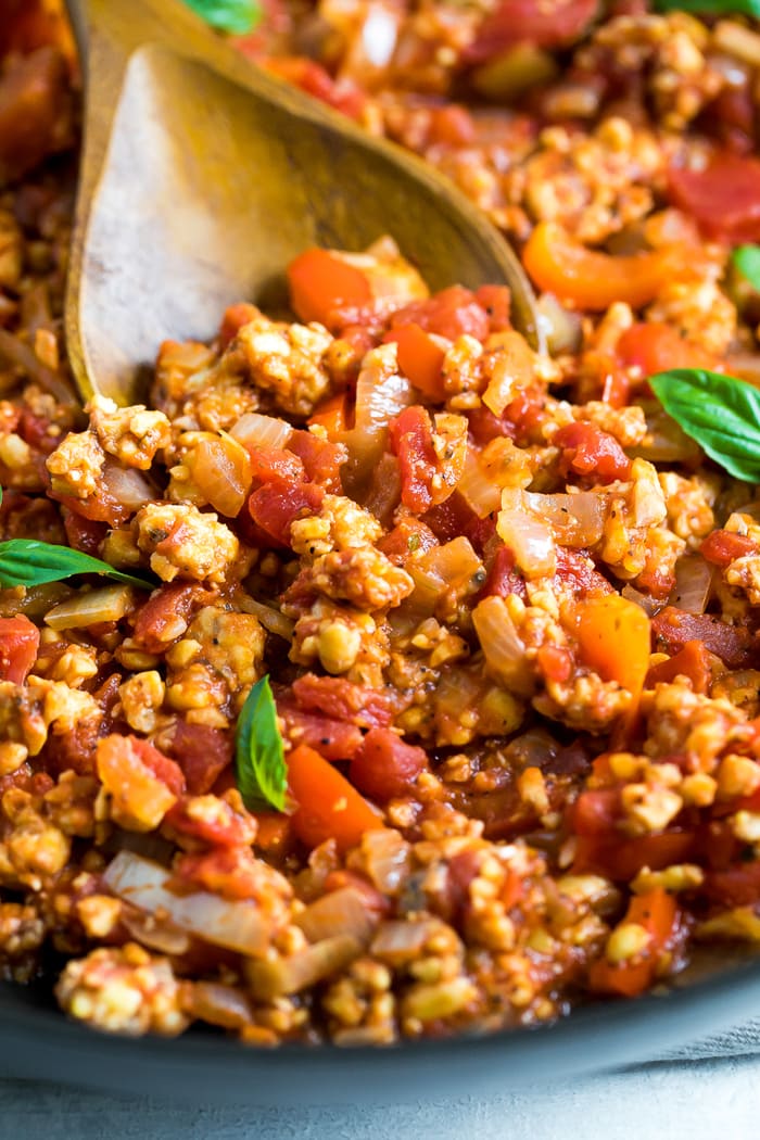 Wooden spoon stirring a pot of tempeh bolognese sauce that is topped with fresh basil.
