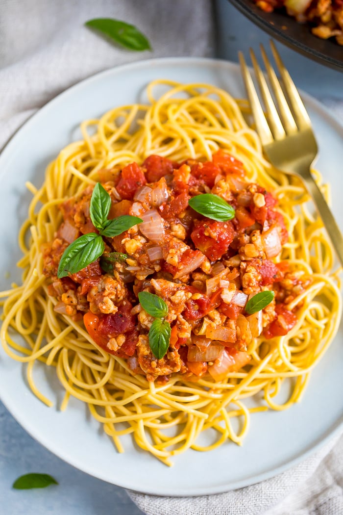 Plate of spaghetti topped with tempeh bolognese sauce and fresh basil.