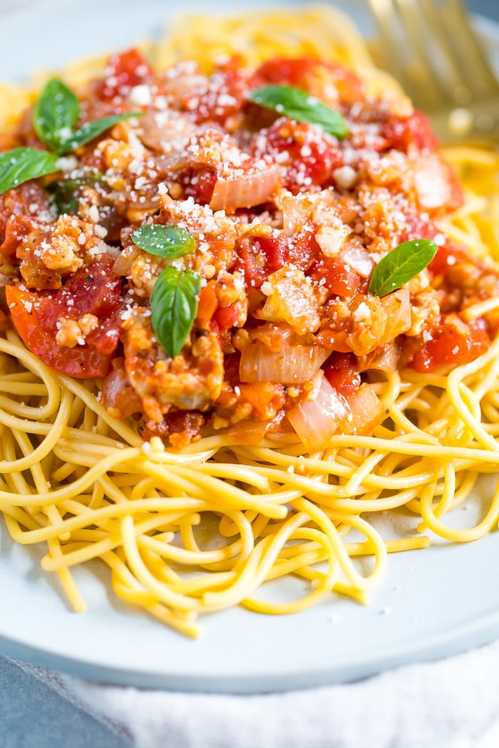 Plate of spaghetti topped with tempeh bolognese sauce, parmesan, and fresh basil.