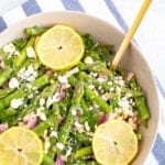 Bowl of asparagus salad with lemon slices, feta, and chopped red onion.