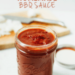 Healthy Homemade BBQ Sauce in a glass jar. Cutting board with knife in the background.