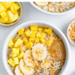 Bowl of overnight oats topped with pineapple, mango, coconut, banana and peanut butter.