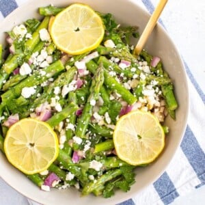 Asparagus feta salad in a large bowl with a gold spoon and lemon slices on top.