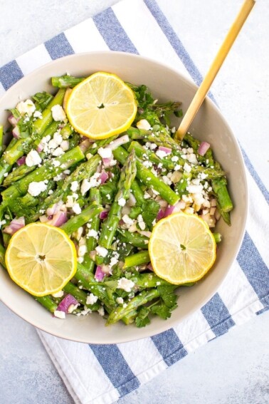 Asparagus feta salad in a large bowl with a gold spoon and lemon slices on top.