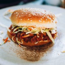 Hearts of palm bbq sandwich with slaw on a sesame seed bun on a white plate.