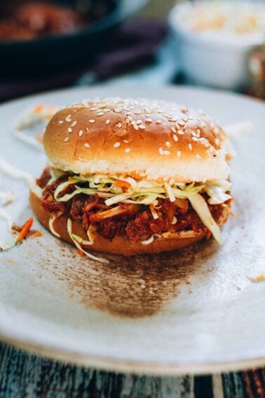 Hearts of palm bbq sandwich with slaw on a sesame seed bun on a white plate.