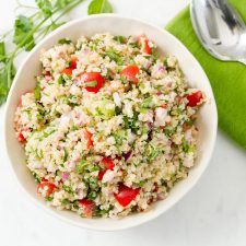 Bowl filled with quinoa tabbouleh and a serving spoon-- quinoa, parsley, tomatoes and onions.