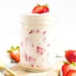 Jar of strawberry shortcake overnight oats with chunks of strawberries and topped with sliced strawberries.
