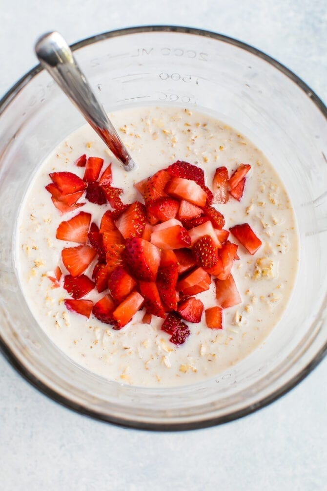 Glass mixing bowl with overnight oatmeal and chopped strawberries