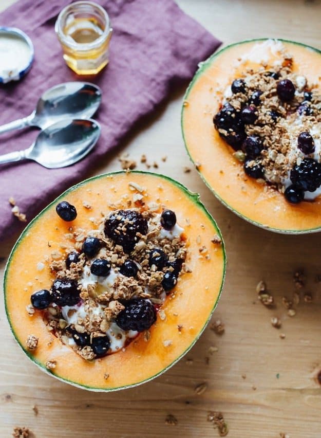 Cantaloupe breakfast bowls filled with yogurt, granola, berries and a drizzle of honey. 