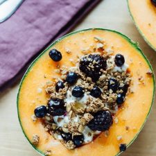 Cantaloupe breakfast bowls filled with yogurt, granola, berries and a drizzle of honey.