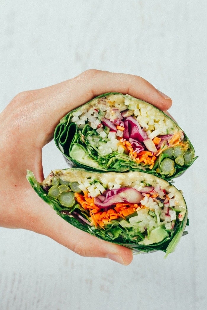 Hand holding two halves of veggie packed hummus collard wraps.