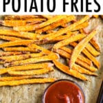 Crispy baked sweet potato fries on parchment paper next to a small bowl of ketchup.