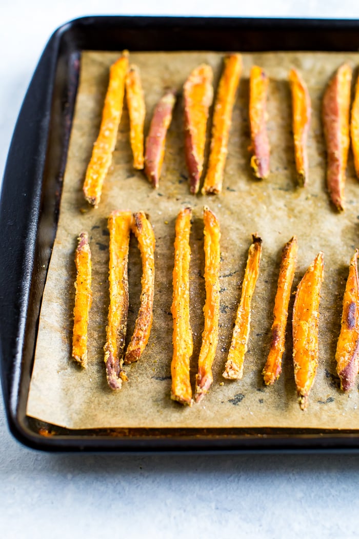 Crispy sweet potato fries lined up on a baking sheet lined with parchment paper.