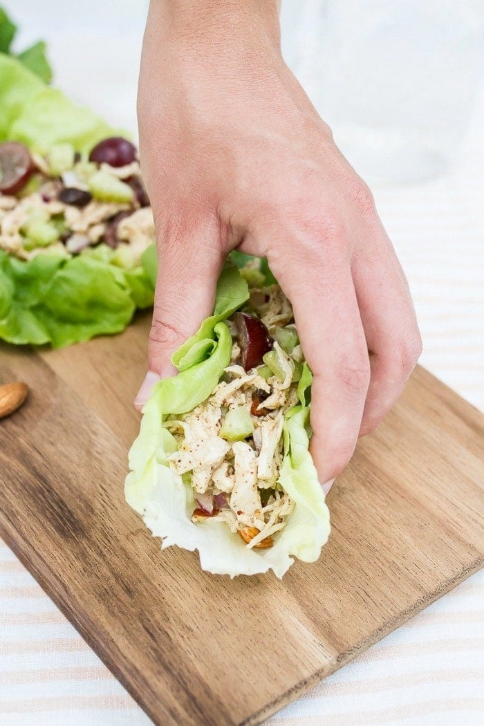 Almond butter chicken salad made with almonds, celery and grapes in lettuce cups. Hand picking up a lettuce cup.