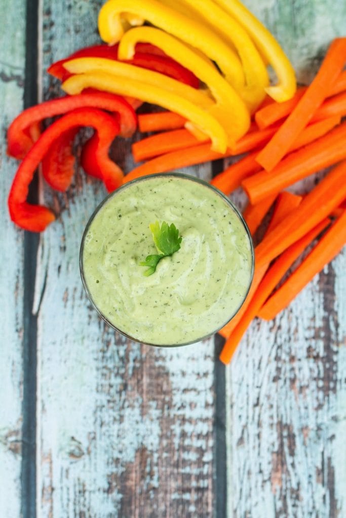 Avocado ranch dressing in a jar next to carrot sticks and pepper slices.