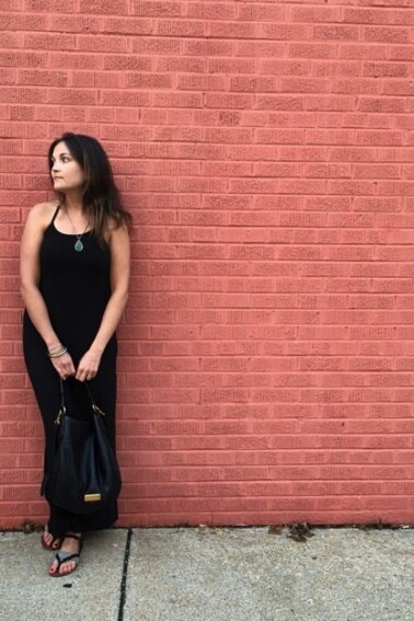 A woman wearing a black maxi-dress against a red brick wall.