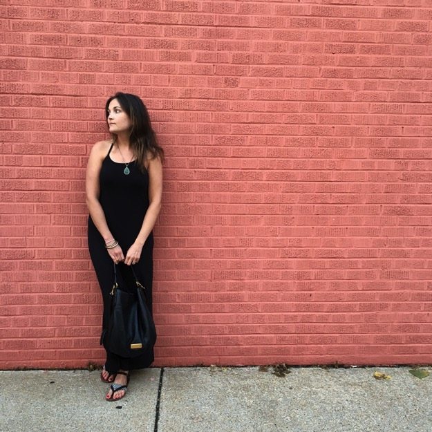 Girl dressed in all black standing against a red brick wall. 