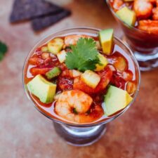 Mexican shrimp cocktail in a small glass with red background.