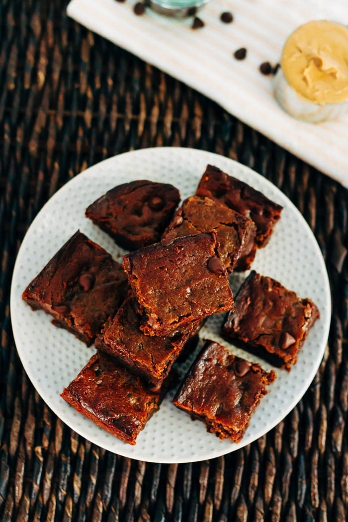 A fun take on traditional brownies, these flourless peanut butter hummus brownies are gooey, chocolatey and absolutely delicious. No flour or oil needed! An overhead photo of a plate with peanut butter hummus brownies stacked on top.