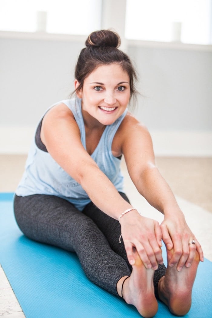Girl sitting on blue yoga mat stretching.