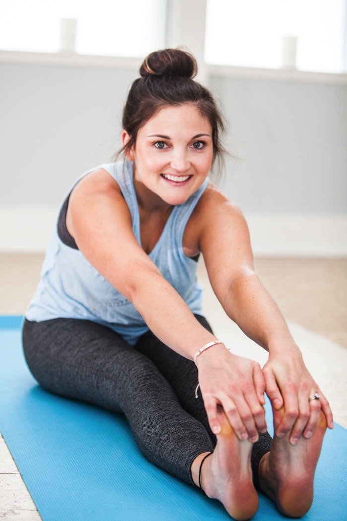 Girl sitting on blue yoga mat stretching.