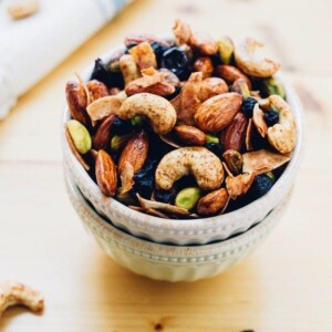 Two bowls stacked, full of trail mix with mixed nuts and dried blueberries.