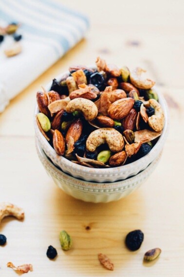 Two bowls stacked, full of trail mix with mixed nuts and dried blueberries.