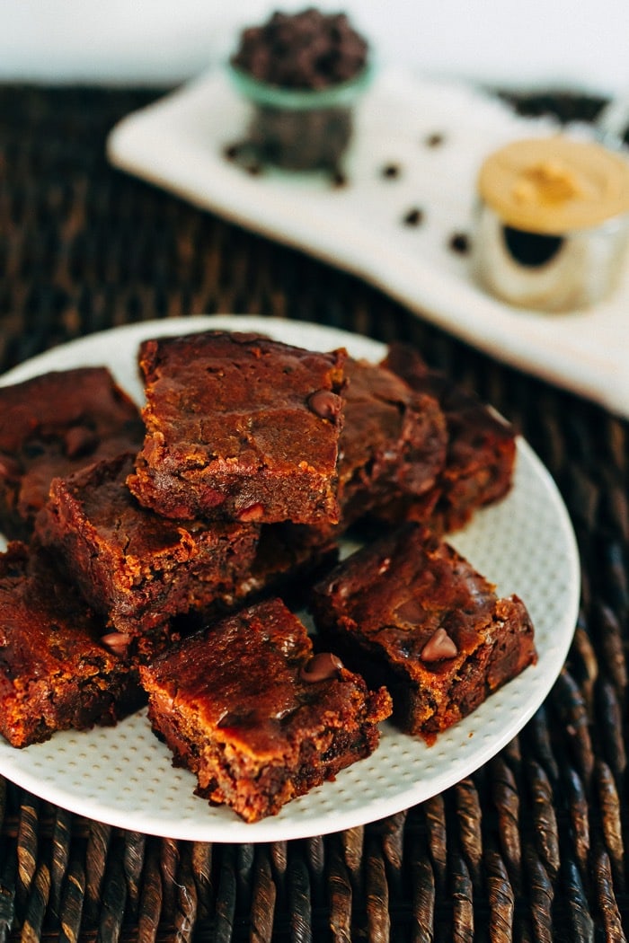 A fun take on traditional brownies, these flourless peanut butter hummus brownies are gooey, chocolatey and absolutely delicious. No flour or oil needed! A plate with peanut butter hummus brownies stacked on top.