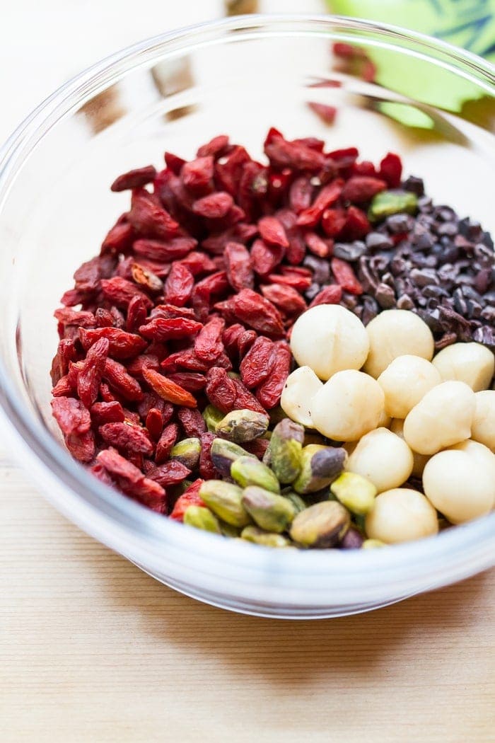 Snack healthy with this crunchy, vibrant pistachio trail mix. It’s a delicious blend of roasted pistachios, macadamia nuts, goji berries and cacao nibs. A bowl of ingredients for pistachio trail mix.