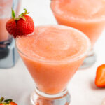 Two glasses with strawberry frosé. Each one has a strawberry on the rim.