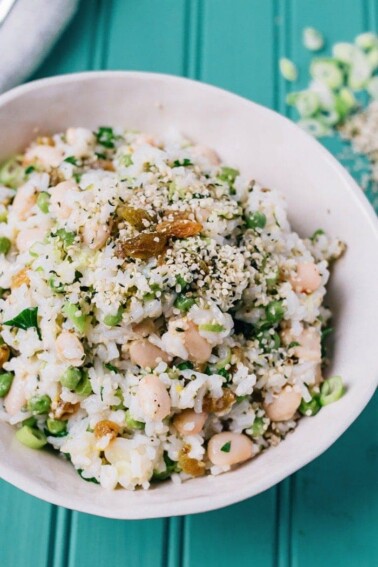 Lemony rice salad with beans, green onion and sesame seeds on a teal table.