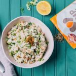 Lemony rice salad with beans, green onion, golden raisins and sesame seeds on a teal table with half a lemon in the background.