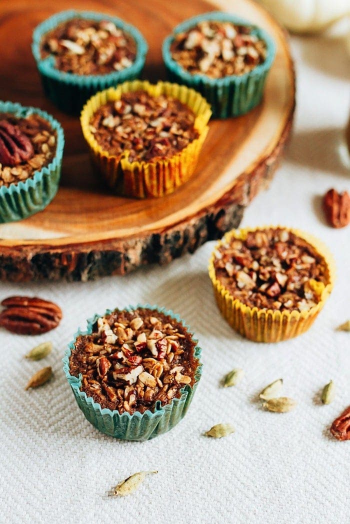 Chai oatmeal cups in cupcake liners on a table and a wooden trivet. Nuts and spices sprinkled around.
