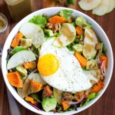 Fall breakfast salad in a bowl with apples, avocado, squash, onion, and walnuts on greens.