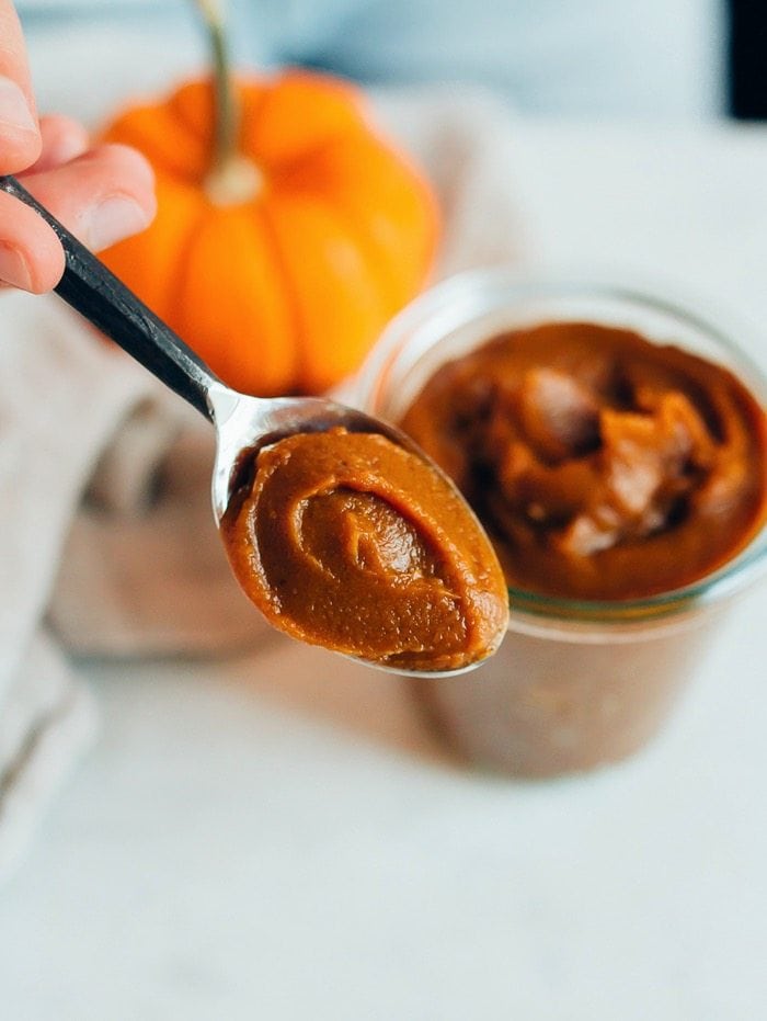 A spoon of pumpkin butter with a jar and pumpkin in the background.