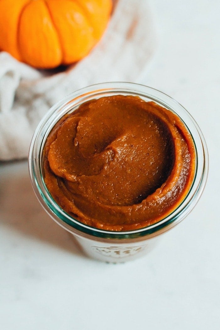 Pumpkin butter in a glass jar with a pumpkin in the background.