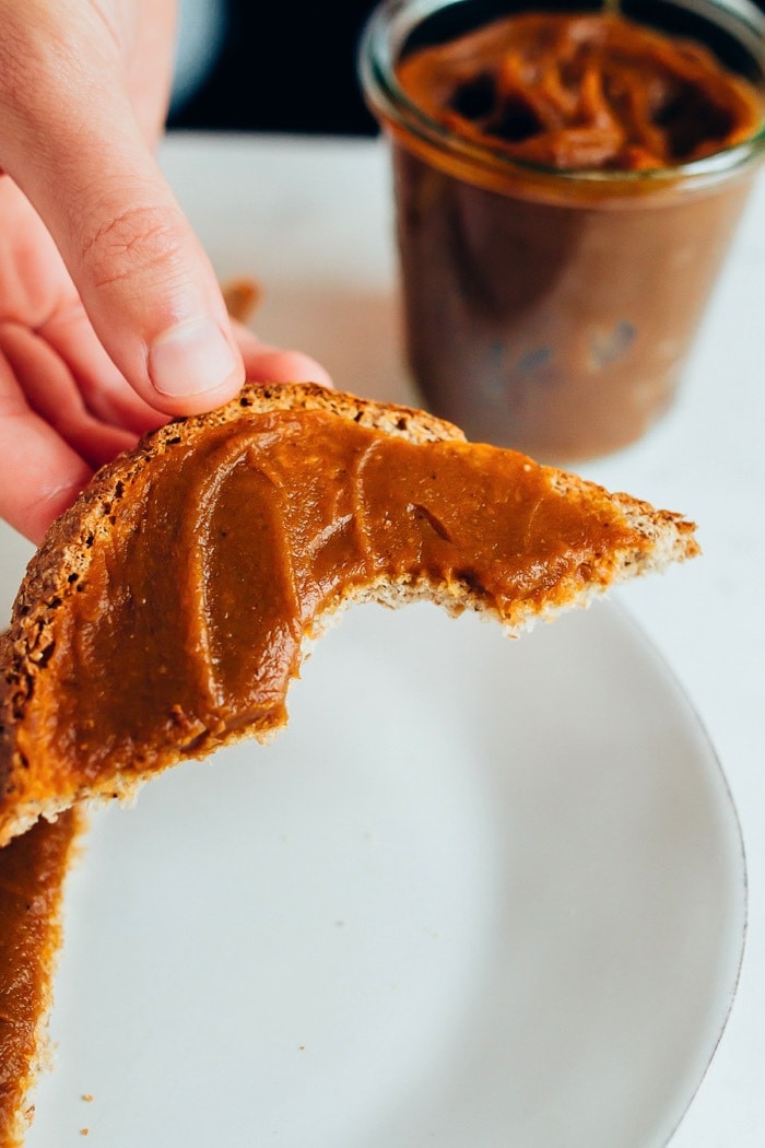 Hand holding a piece of toast with pumpkin butter spread on it.