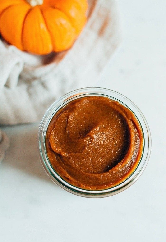 Pumpkin butter in a glass jar, next to a kitchen town and mini pumpkin.